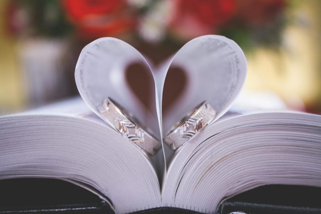 Close-up of wedding rings on heart-shaped book pages symbolizing love and romance.