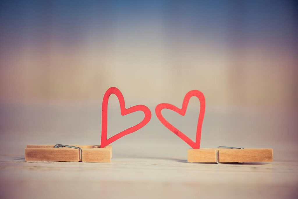 Two wooden clothespins with red heart shapes, symbolizing love and romance, on a blurred background.